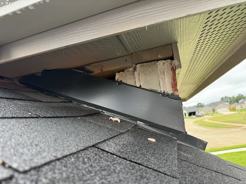 A gap above the roof-to-wall flashing of a new home, with broken brick visible behind it